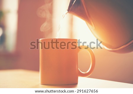 kettle pouring boiling water into a cup in morning sunlight