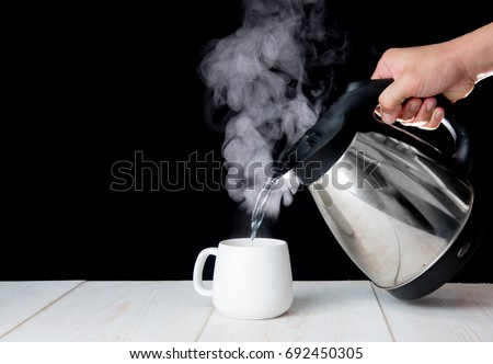 kettle pouring boiling water into a cup with smoke on wood table