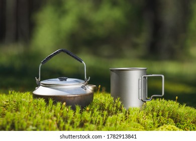 Kettle And Titanium Mug On Green Moss. The Background Is Blurry.