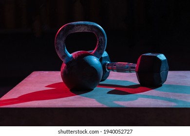 Kettlebell and dumbbell in red-blue gradient light on dark background