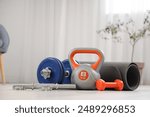 Kettlebell with dumbbells and fitness mat in living room, closeup