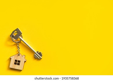 Key chain in the shape of wooden house with key on a yellow background. Building, design, project, moving to new home, mortgage, rent and purchase real estate. Copy space