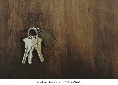 Key Chain With Three House Or Door Keys On A Dark Wood Table Top.