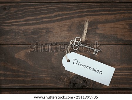 The key of dissension  concept isolate. Silver key with a label on wood table.