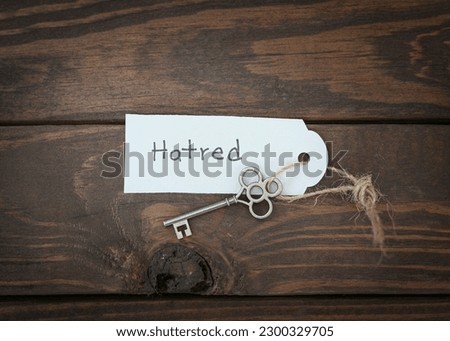 The key of hatred concept isolate. Gold key with a label on wood table.