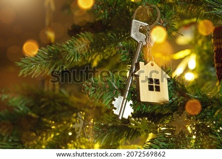 Key to the house with a keychain is hanging on the Christmas tree. A gift for New Year, Christmas. Building, design, project, moving to new house, mortgage, rent and purchase real estate. Copy space