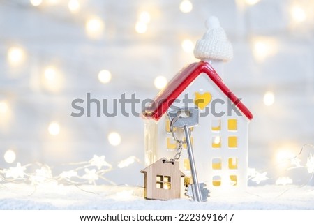 Key to the house with a keychain on a cozy home with a Christmas decor. A gift for New Year, Christmas. Building, design, project, moving to new house, mortgage, rent and purchase real estate
