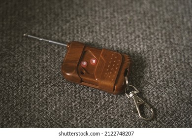 Key And Keychain With Buttons And Brown Alarm For A Car On A Gray Sofa. 