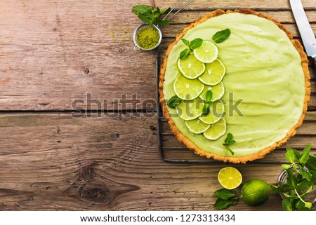 Key Lime Pie with several limes and mint over wooden background, top view with copy space.