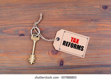 Key and a note on a wooden table with text - Tax Reforms