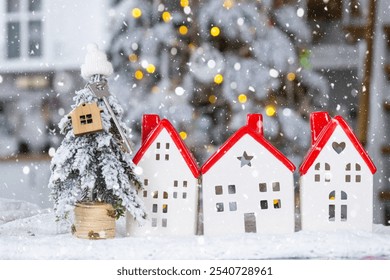 Key on Christmas tree and tiny house with a red roof with Christmas decor on table of festive white kitchen. Gift for New Year. Insurance, moving to new house, mortgage, rent and real estate