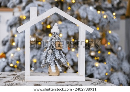 Key on Christmas tree and tiny house on cozy home with Christmas decor on table of festive white kitchen. Gift for New Year. Insurance, moving to new 