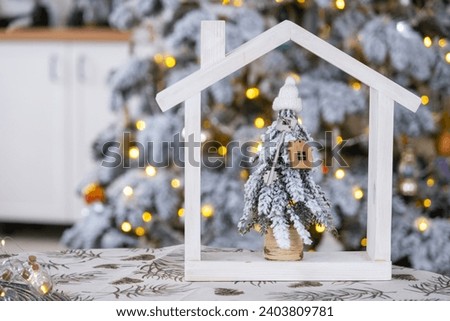 Key on Christmas tree and tiny house on cozy home with Christmas decor on table of festive white kitchen. Gift for New Year. Insurance, moving to new house, mortgage, rent and real estate