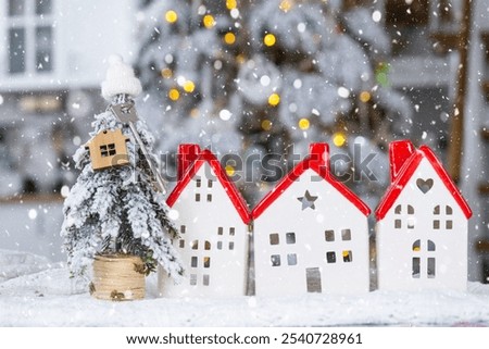 Key on Christmas tree and tiny house with a red roof with Christmas decor on table of festive white kitchen. Gift for New Year. Insurance, moving to new house, mortgage, rent and real estate