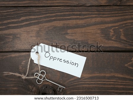 The key of oppression  concept isolate. Silver key with a label on wood table.