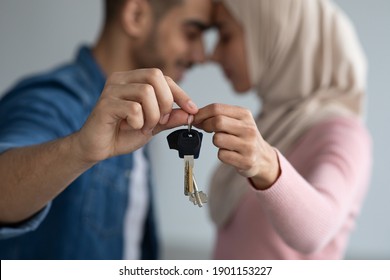 Key in romantic muslim couple hands, closeup. Loving middle eastern man and woman in hijab bonding and holding key from their new house together, selective focus. Moving, real estate concept
