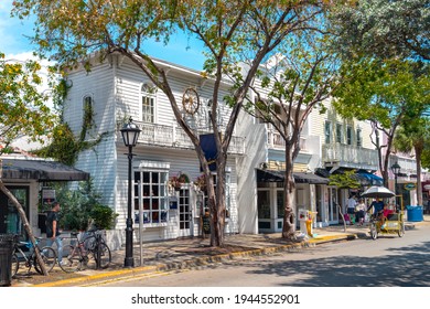 Key West, USA - 04.30.2017: Duval Street In Wooden District On A Sunny Day With Trees, Colorful Wooden Houses.  People Walking And Cycling By. Sunny Day In Vintage Neighborhood. Carribean Vibe.