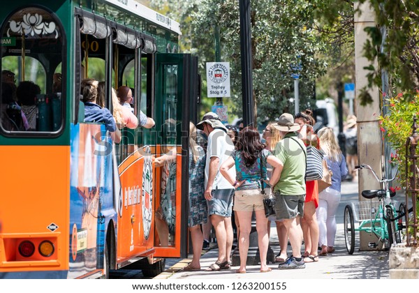 Key West, USA - May 1, 2018: Back view of old town\
trolley best guided tourist tour bus with people, tourists\
boarding, getting on, off, sitting at stop on street, road in\
Florida island city keys