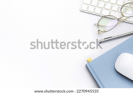 Keyboard, computer mouse and notebook with pen on white office desk.  Directly above shot of office desk and stationery on white background