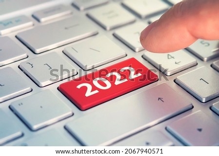 Keyboard with text HAPPY 2022 and finger pushing the enter button. Color button on the gray silver keyboard of modern ultrabook. caption on the button