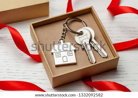 Keychain house and keys with red ribbon and gift box on white wooden background