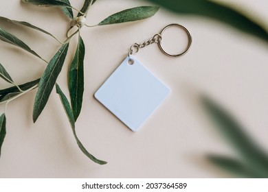 Keychain mockup among olive leaves to display design. Blank white sublimation key chain photo. Flat lay, top view.