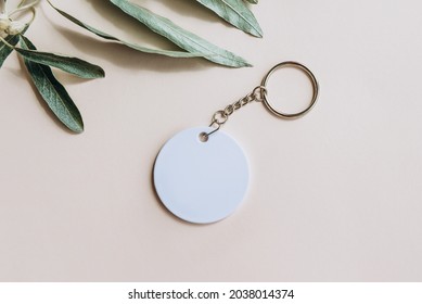 Keychain Mockup Among Olive Leaves To Display Design. Blank White Sublimation Key Chain Photo. Flat Lay, Top View.