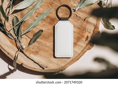 Keychain mockup among olive leaves to display design. Blank white sublimation key chain photo. Flat lay, top view.
