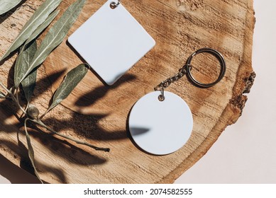 Keychain Mockup Among Olive Leaves To Display Design. Blank White Sublimation Key Chain Photo. Flat Lay, Top View.