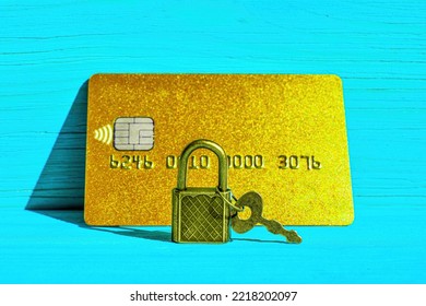 Keyed Padlock In Front Of A Golden Credit Card Placed On A Blue Wooden Background. Financial Fraud Protection Concept.