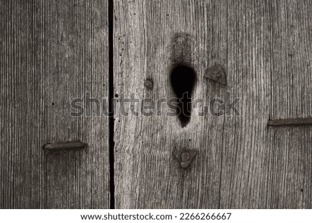 Keyhole on grey old weathered wooden door with paint peeling off. Fragment of old wooden door without handle. 