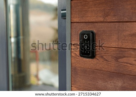 Keyless entry system mounted on wooden wall beside glass door, device is easily accessible