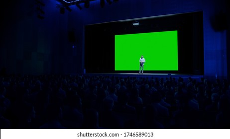 Keynote Speaker Does Presentation Of New Product To The Audience, Behind Him Movie Theater With Green Screen, Mock-up, Chroma Key. Business Conference Live Event Or Device Reveal