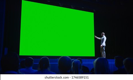 Keynote Speaker Does Presentation Of New Product To The Audience, Behind Him Movie Theater With Green Screen, Mock-up, Chroma Key. Business Conference Live Event Or Device Reveal