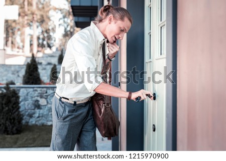 Keys in hand. Stylish man holding keys in his hand and speaking by the phone while opening the door to his house