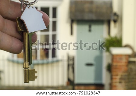 Keys to a home with a house shaped key ring and an english country cottage in the background
