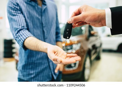 Keys From New Car, Young Salesman Transfer The Car Key In Hand Of Customer In Casual Wear On Dealership Background