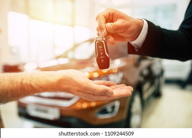 Keys From New Car, Young Salesman Transfer The Car Key In Hand Of Customer In Casual Wear On Dealership Background