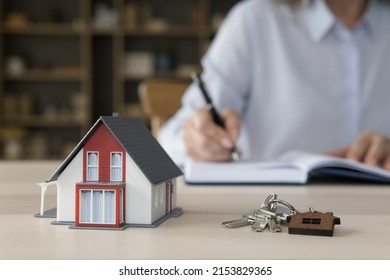 Keys from new home and tiny model of family house on work table of realtor, agent, developer. Property seller, buyer, renter writing notes in notebook, offering support in selling, buying apartment