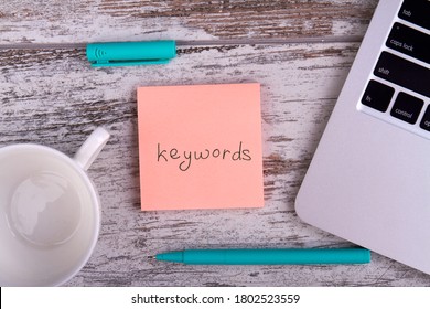 Keywords for web optimization. Pen, white cup and laptop on wooden table.