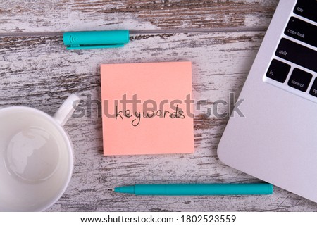 Keywords for web optimization. Pen, white cup and laptop on wooden table.