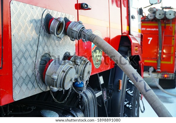 Khabarovsk, Russia - January 1, 2021, emblem fire\
service,\
stock Russian fire truck, red and white, tank truck with\
connected fire hose, flowing water and spray, in winter snow\
season, hydrant