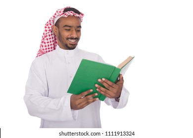 Khaleeji man wearing a thobe, holding an open book reading it and smiling, isolated on white background.