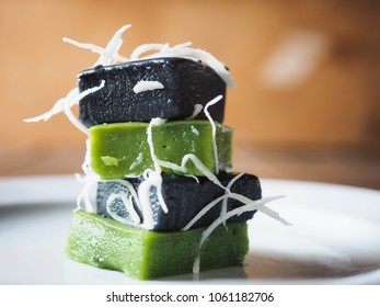 KHANOM PIAK POON, Black and Green Thai coconut milk sweet pudding with coconut shreds on top. Color from pandan leaf and charred coconut coir. Tower of dessert on white plate. - Shutterstock ID 1061182706