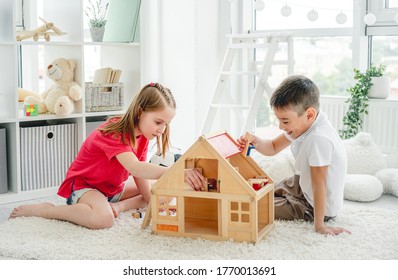 Kharkiv, Ukraine - 06 June 2020: Cute little boy and girl playing with wooden doll house indoors