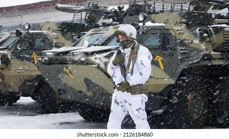 Kharkiv, Ukraine - January, 31, 2022: A soldier in white camouflage with a weapon stands near an armored personnel carrier in winter. Ukrainian army prepares to defend against Russian invasion