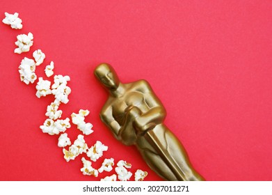 KHARKIV,UKRAINE - JULY 1, 2020: Plastic Oscar award on a red background with popcorn.