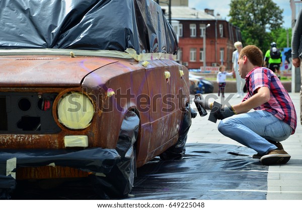 KHARKOV,\
UKRAINE - MAY 27, 2017: Festival of street art. Young guys draw\
graffiti on the car body in the city center. The process of drawing\
color graffiti on a car with aerosol\
cans