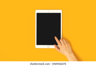 Kharkov, Ukraine - May 5, 2021: Woman Hand Touch Apple IPad Screen, Person Using Digital Tablet With Mockup Screen, Yellow Background And Top View 