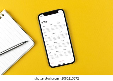 Kharkov, Ukraine - November 17, 2021: Calendar for 2022 on Apple iPhone screen. Calendar application. Business workspace with notepad and pen, top view 